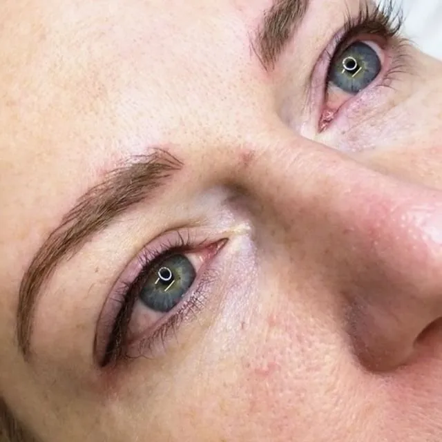 Natural-looking feather-stroke brow tattooing on a client with blue-green eyes