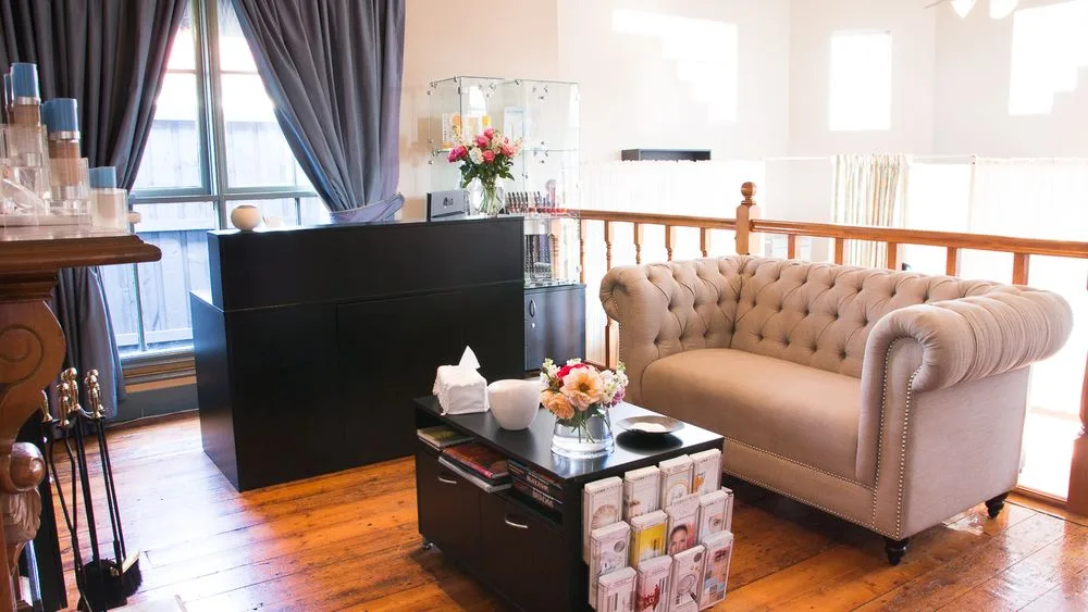 Waiting lounge: buttoned chesterfield on polished floorboards, timber-balustraded stair rail, reception counter with pink roses