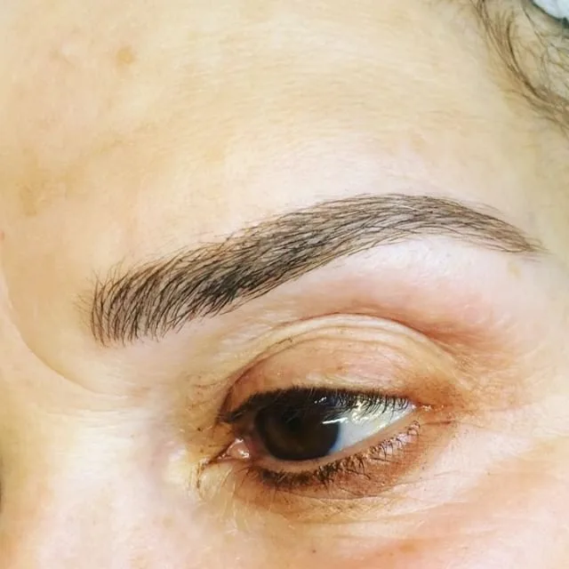 Close-up of a healed feather-stroke tattooed brow on mature skin with soft hair-stroke edge